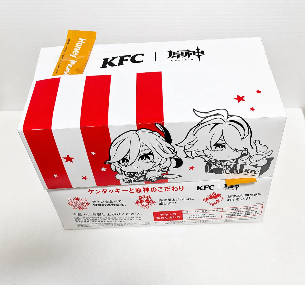 斜め上から撮影したKFC原神コラボ第2弾の特別デザインパッケージ。KFCと原神のロゴ、アルハイゼンとカーヴェのイラストが確認できる持ち帰り用ボックス。